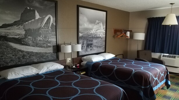 A hotel room with two beds, a large wall-mounted picture, a desk with a lamp, and a window with curtains. - Super 8 by Wyndham Keokuk (Keokuk)