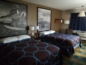 Habitación de hotel con dos camas, un cuadro grande en la pared, un escritorio con lámpara y una ventana con cortinas.