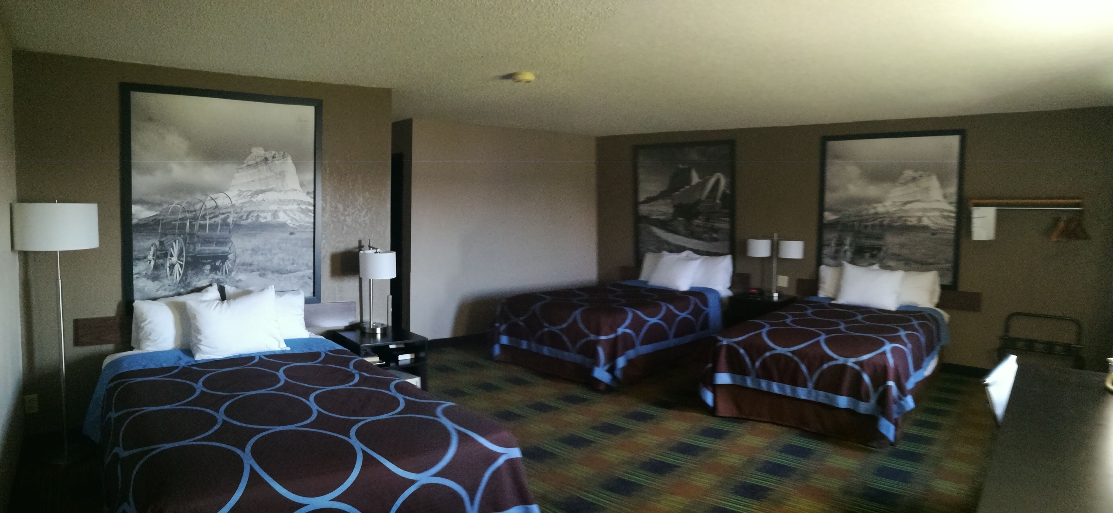 A hotel room with two beds, a desk, and a chair. There are two wall-mounted lamps and a large painting on the wall.