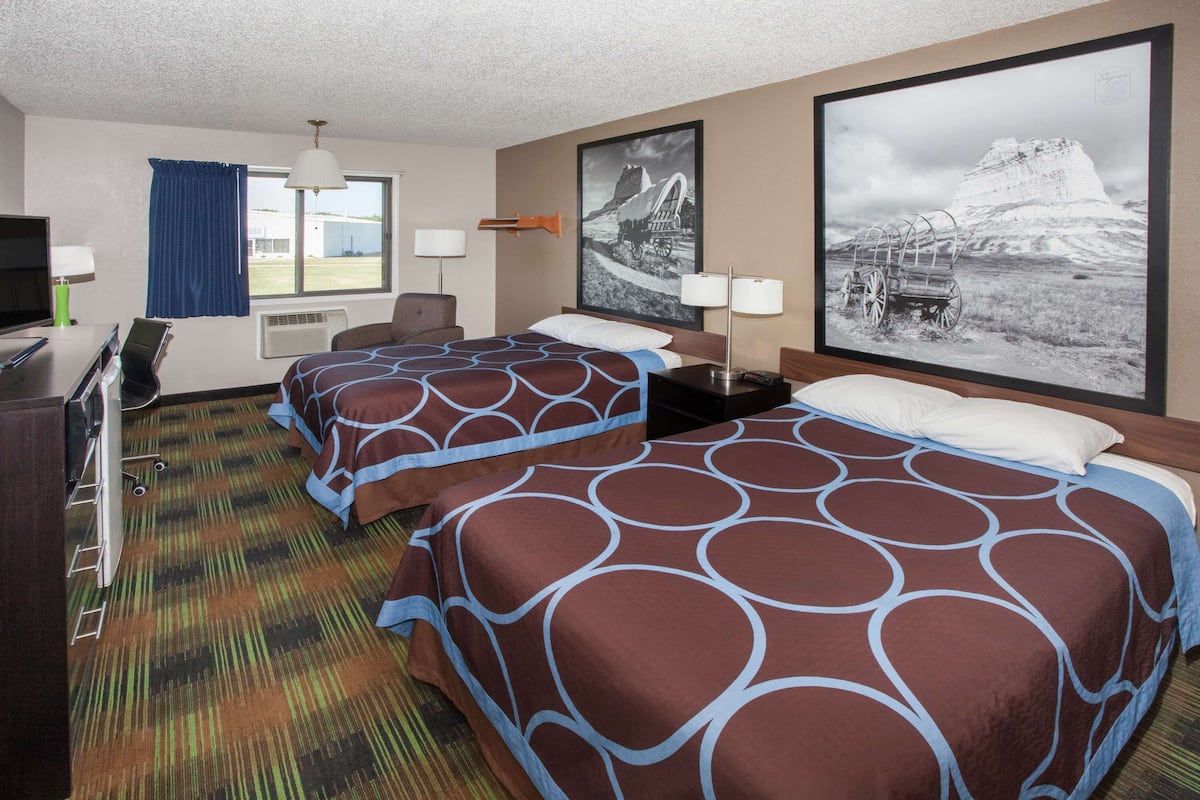 A hotel room with two beds, a desk, a TV, and a large window.