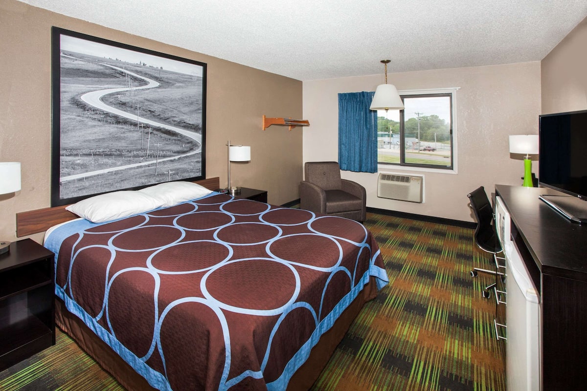 A hotel room with a large bed, a desk, a chair, a television, and a window with curtains.