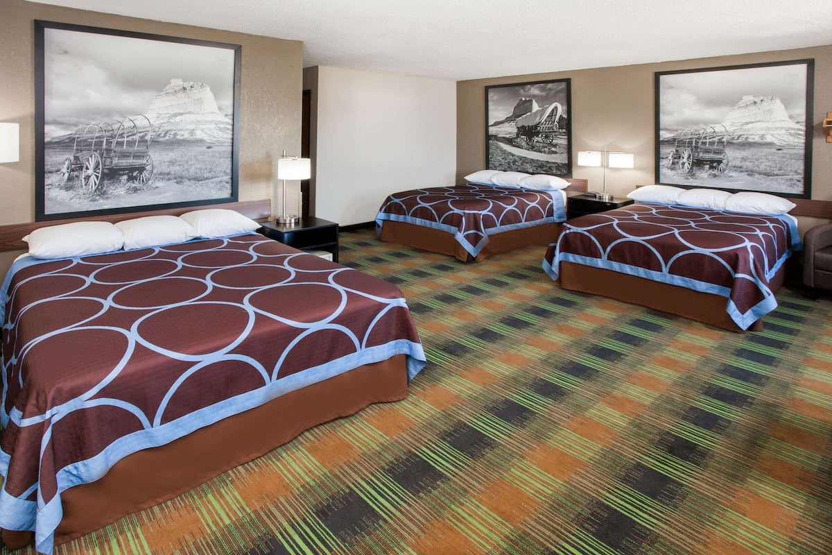 A hotel room with two beds, each with a patterned bedspread and pillows. There are two bedside tables with lamps, and the room has a carpeted floor.