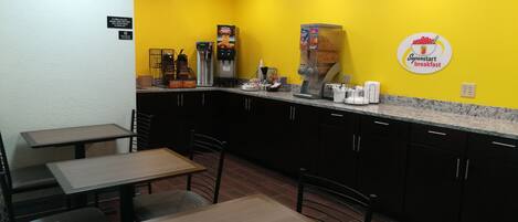 Een klein, kleurrijk café met een gele muur, een koffieapparaat en een bord met 'Superstart ontbijt'.