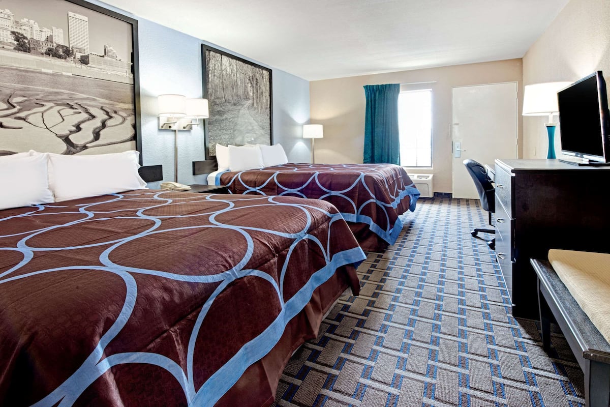 Een hotelkamer met twee bedden, een bureau, een stoel, een televisie en een stadsgezichtschilderij aan de muur.