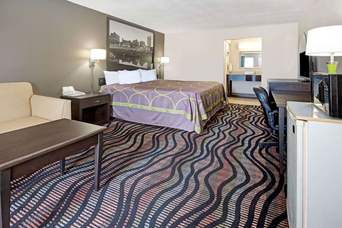 Een hotelkamer met een bed, een bureau, een stoel, een bank, een bureaulamp, een magnetron en een groot raam.