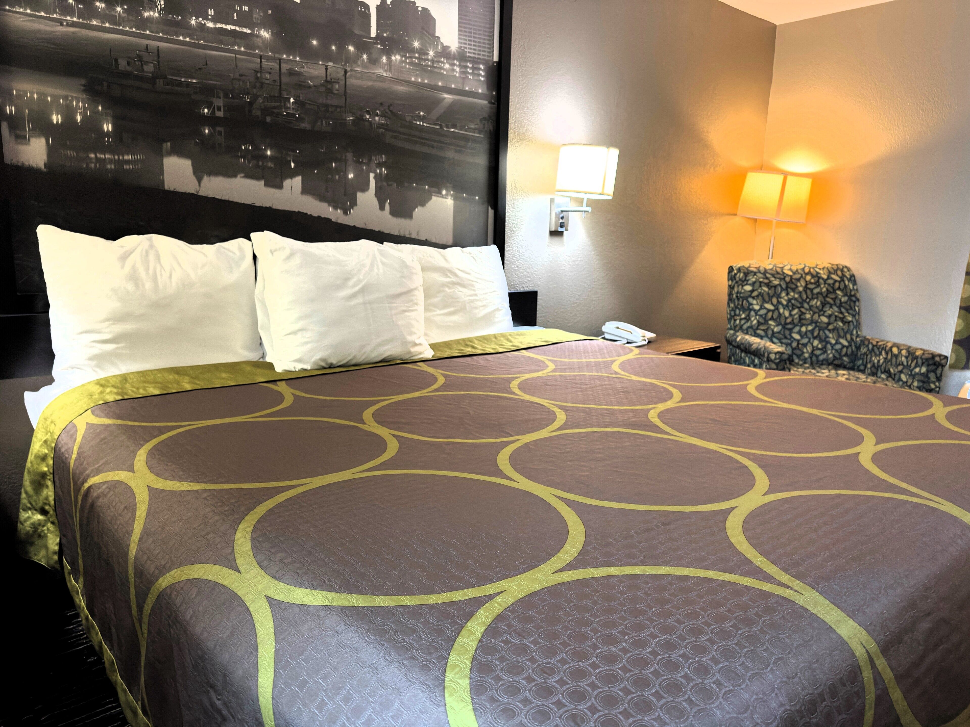 Una habitación de hotel con una cama grande, una mesita de noche, una lámpara y una silla.