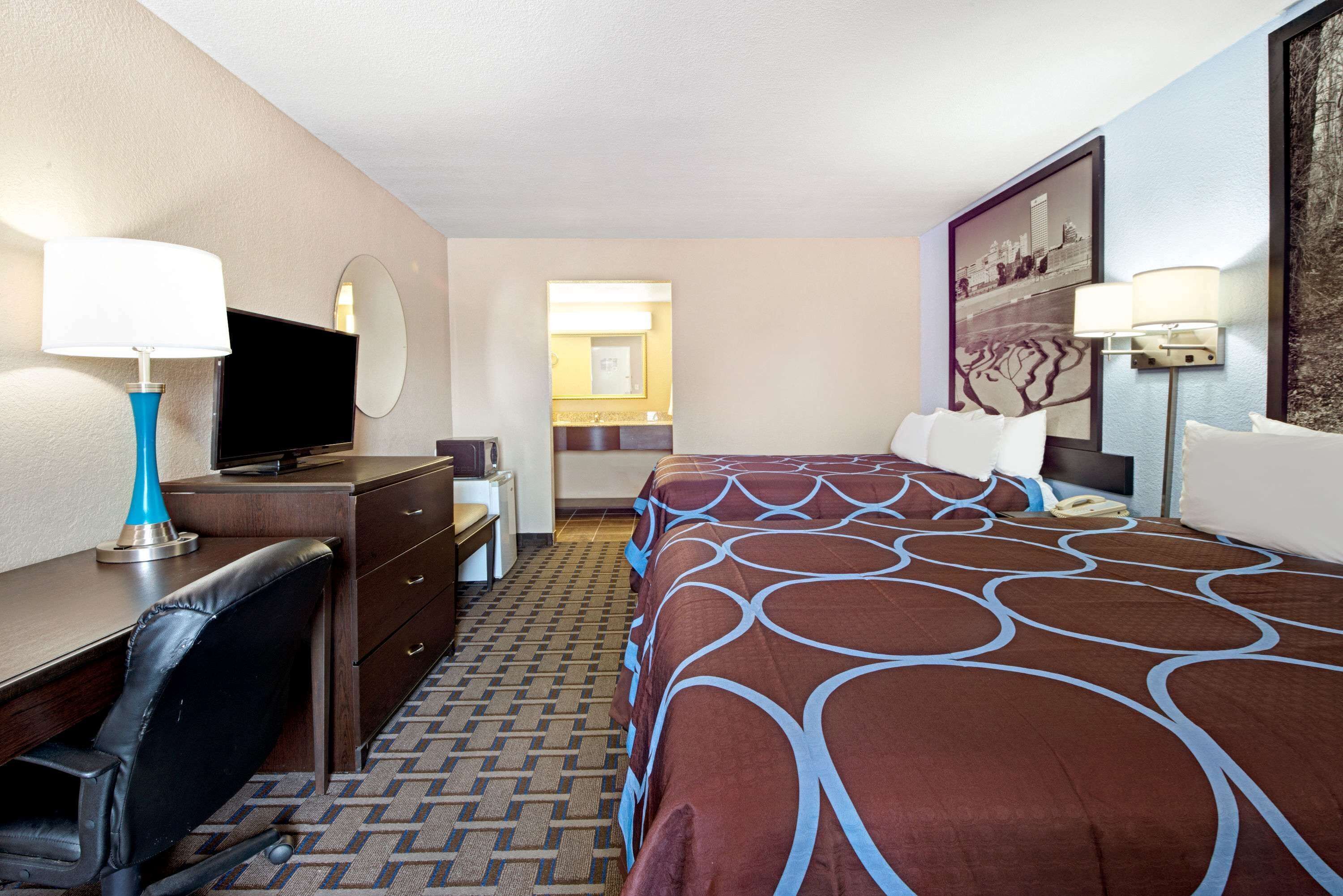 A hotel room with a bed, desk, chair, TV, and two lamps.