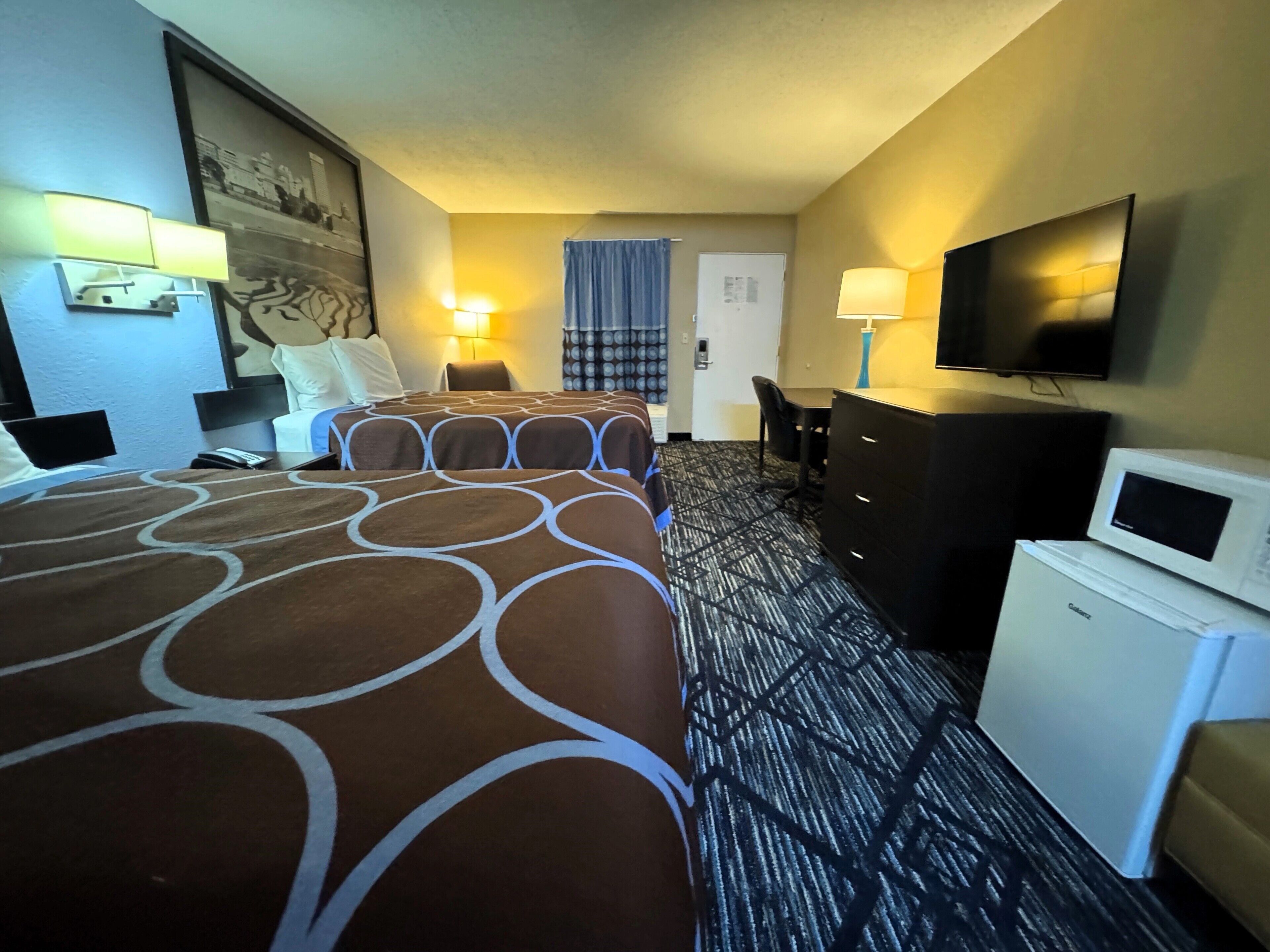 A hotel room with two beds, a desk, a television, and a refrigerator.
