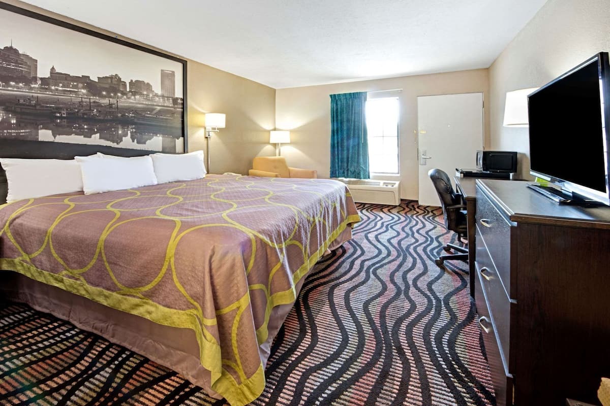 Een hotelkamer met een bed, een bureau, een stoel, een televisie en een groot raam.
