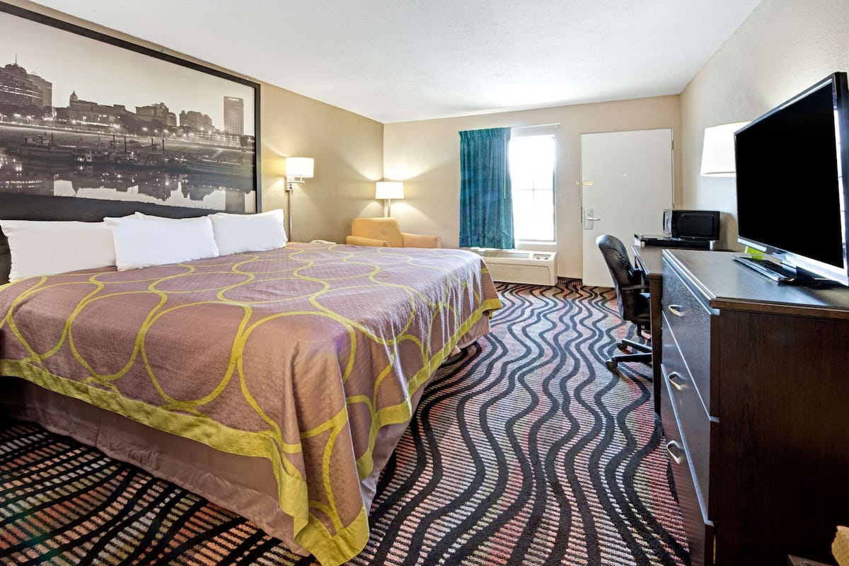 Een hotelkamer met een groot bed, een bureau met een televisie, een stoel en een raam met gordijnen.