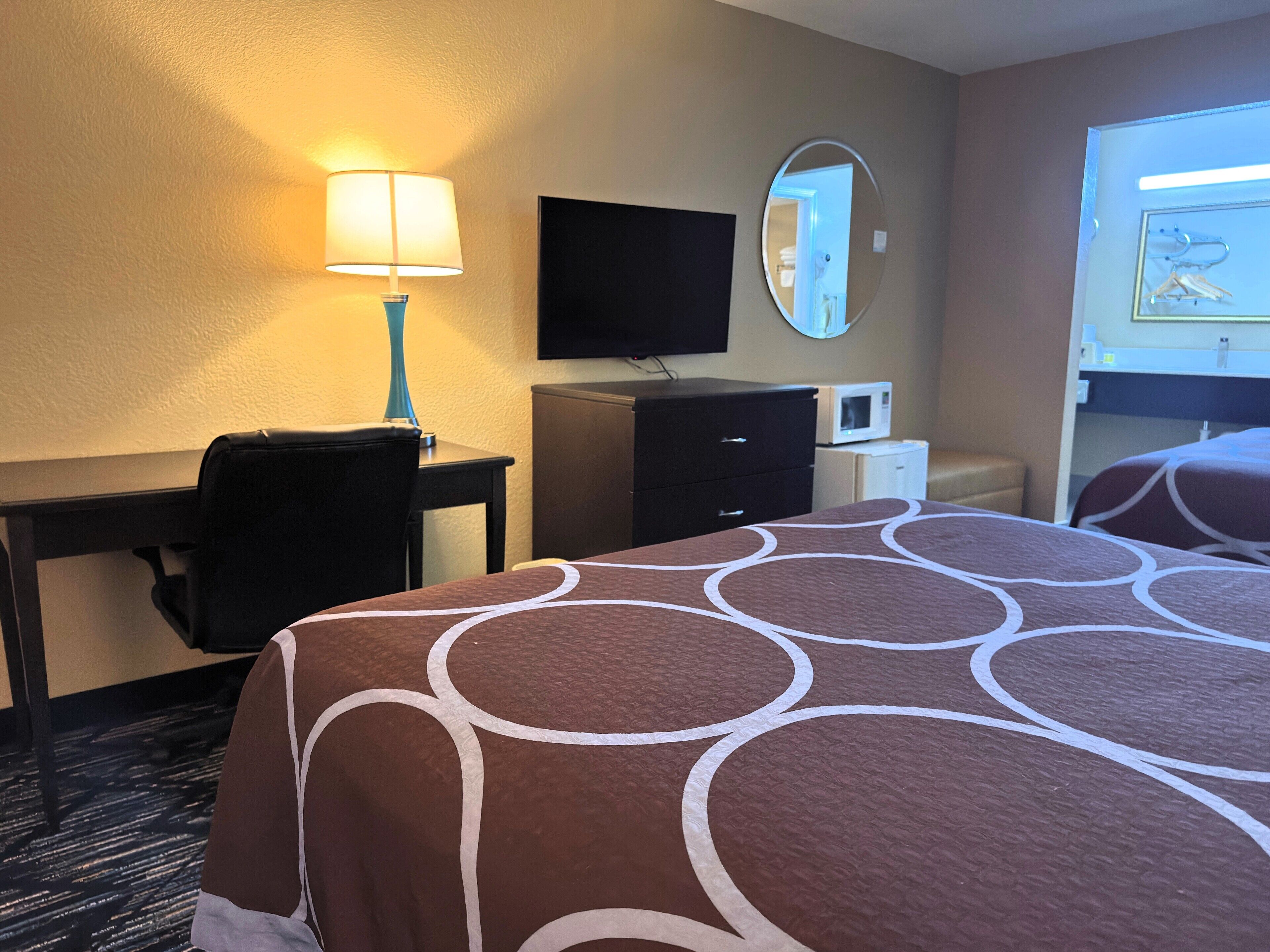 Habitación de hotel con cama, escritorio, silla, televisión, espejo y microondas.