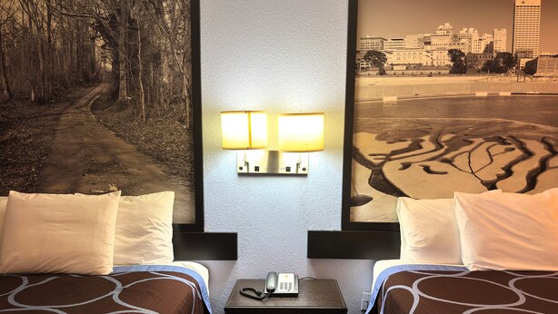 A hotel room with two beds, a nightstand with a phone, and a wall-mounted lamp.