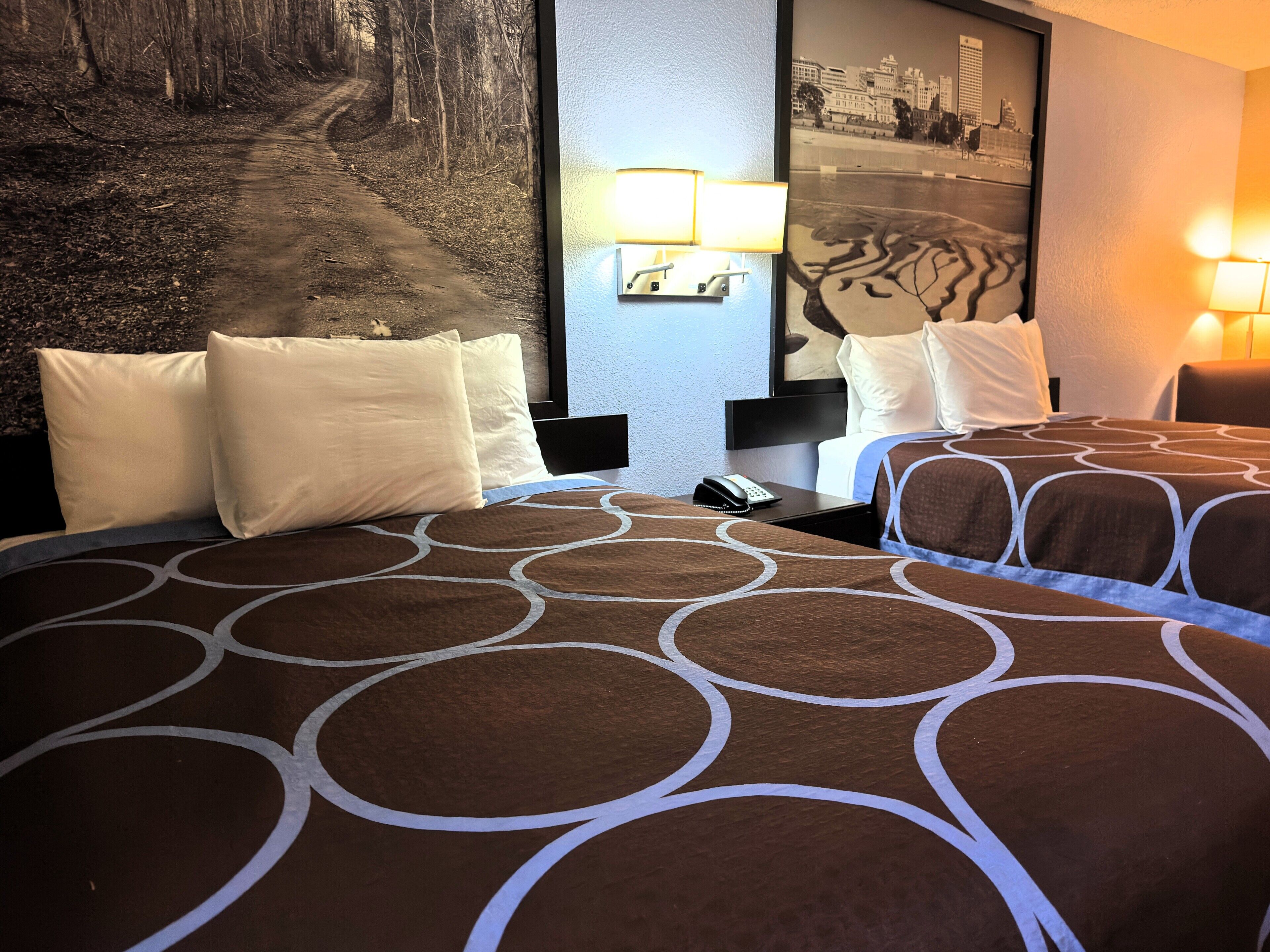 A hotel room with two beds, a nightstand, a phone, and a wall-mounted lamp.