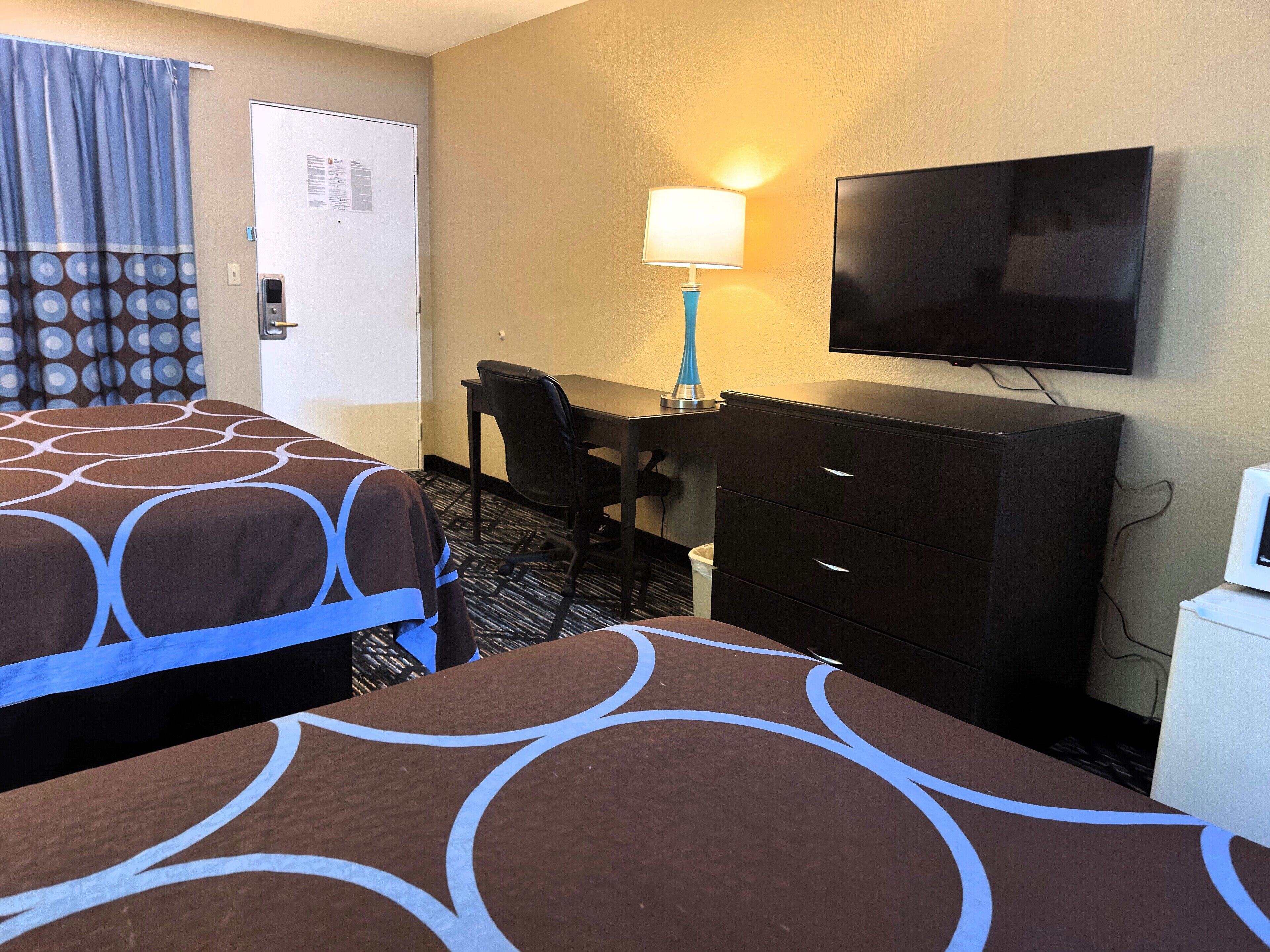 Une chambre d’hôtel avec deux lits, un bureau, une chaise, une télévision et une lampe.