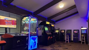 Un espace de jeux équipé de bornes d’arcade, d’un grand jeu de type « machine à gagner » et d’un panneau indiquant le prix pour jouer.