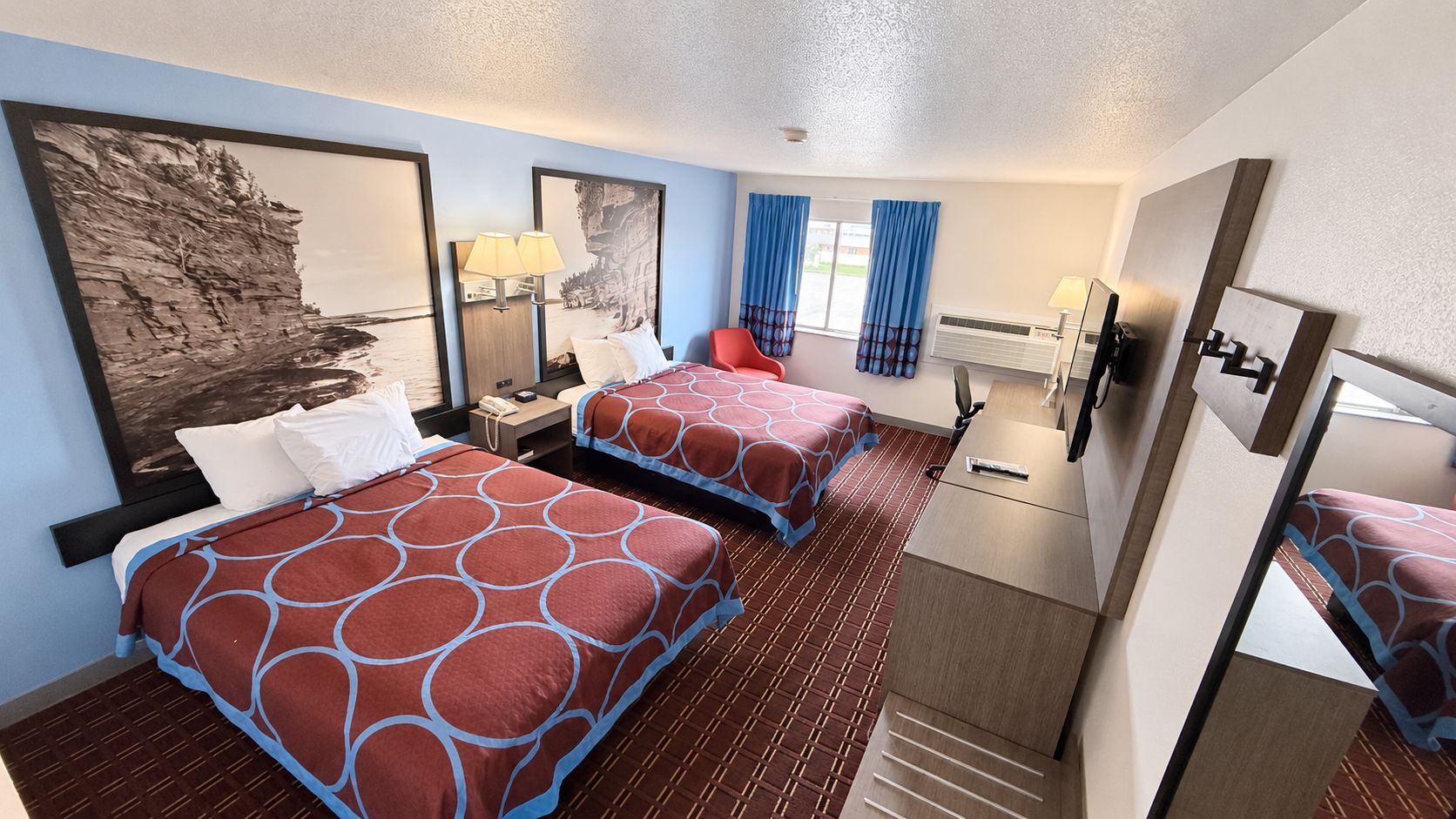 Ein Hotelzimmer mit zwei Betten, einem Schreibtisch, einem Stuhl, einem Spiegel und Bildern an den Wänden.