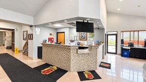 Un espace d’accueil d’hôtel comprenant un comptoir de réception, un téléviseur fixé au mur et un coin café.