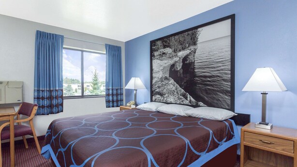 Une chambre d’hôtel avec un grand lit, deux tables de chevet avec des lampes, un bureau avec une chaise, une fenêtre avec des rideaux et un grand tableau mural.