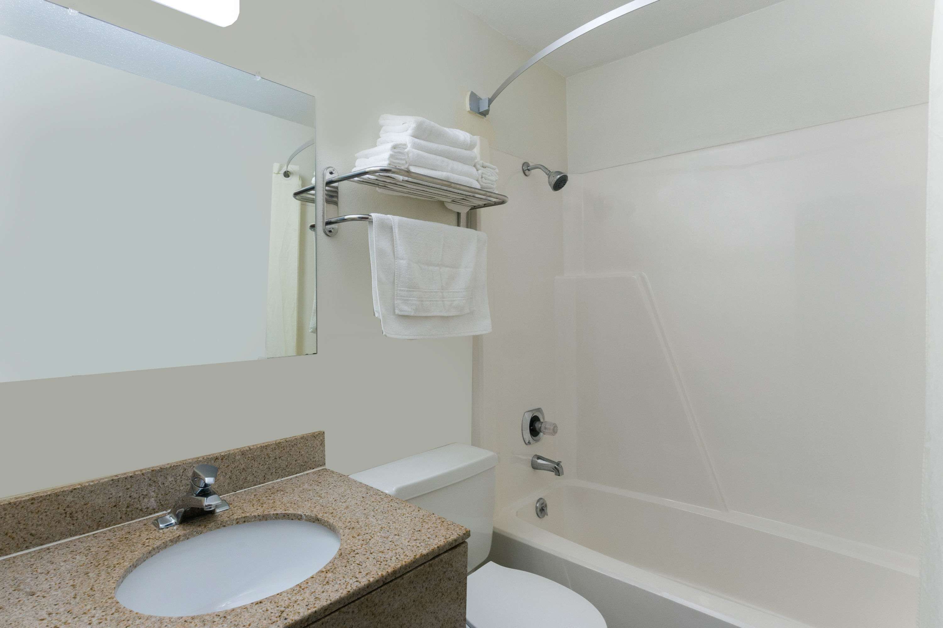 A bathroom with a granite countertop sink, a white toilet, a bathtub, and a towel rack with folded towels.