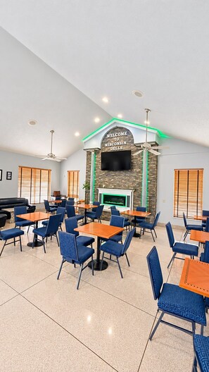 A spacious indoor dining area with multiple tables and chairs, a fireplace, and a television mounted on the wall. - Super 8 by Wyndham Wisconsin Dells (Wisconsin Dells)