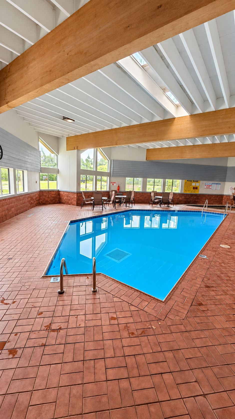 Una piscina interna con pavimento piastrellato blu, circondata da pareti in mattoni e travi in legno.