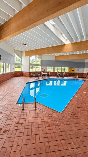 An indoor swimming pool with a blue tiled floor, surrounded by brick walls and wooden beams. - Super 8 by Wyndham Wisconsin Dells (Wisconsin Dells)