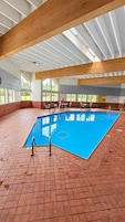 An indoor swimming pool with a blue tiled floor, surrounded by brick walls and wooden beams.