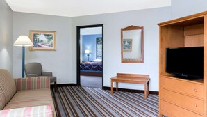 A hotel room with a striped carpet, a sofa, a chair, a wooden table, a TV on a wooden cabinet, and framed pictures on the walls. - Super 8 by Wyndham Wisconsin Dells (Wisconsin Dells)