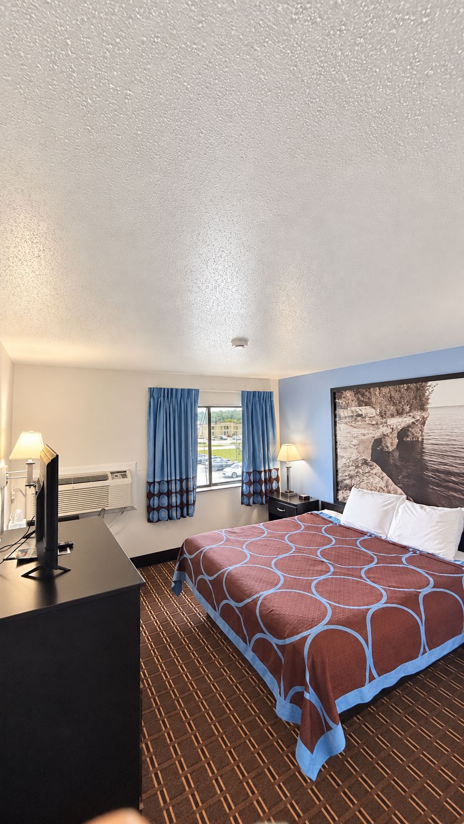 A hotel room with a bed, a desk, a television, and a window with curtains.