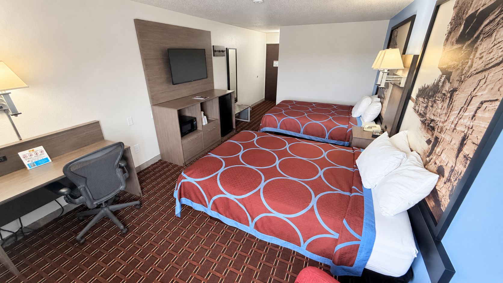 Habitación de hotel con dos camas, un escritorio, una silla, un televisor y la puerta del baño.