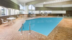 Une piscine intérieure avec un revêtement de sol en carrelage, des chaises de piscine en métal blanc et des tables.