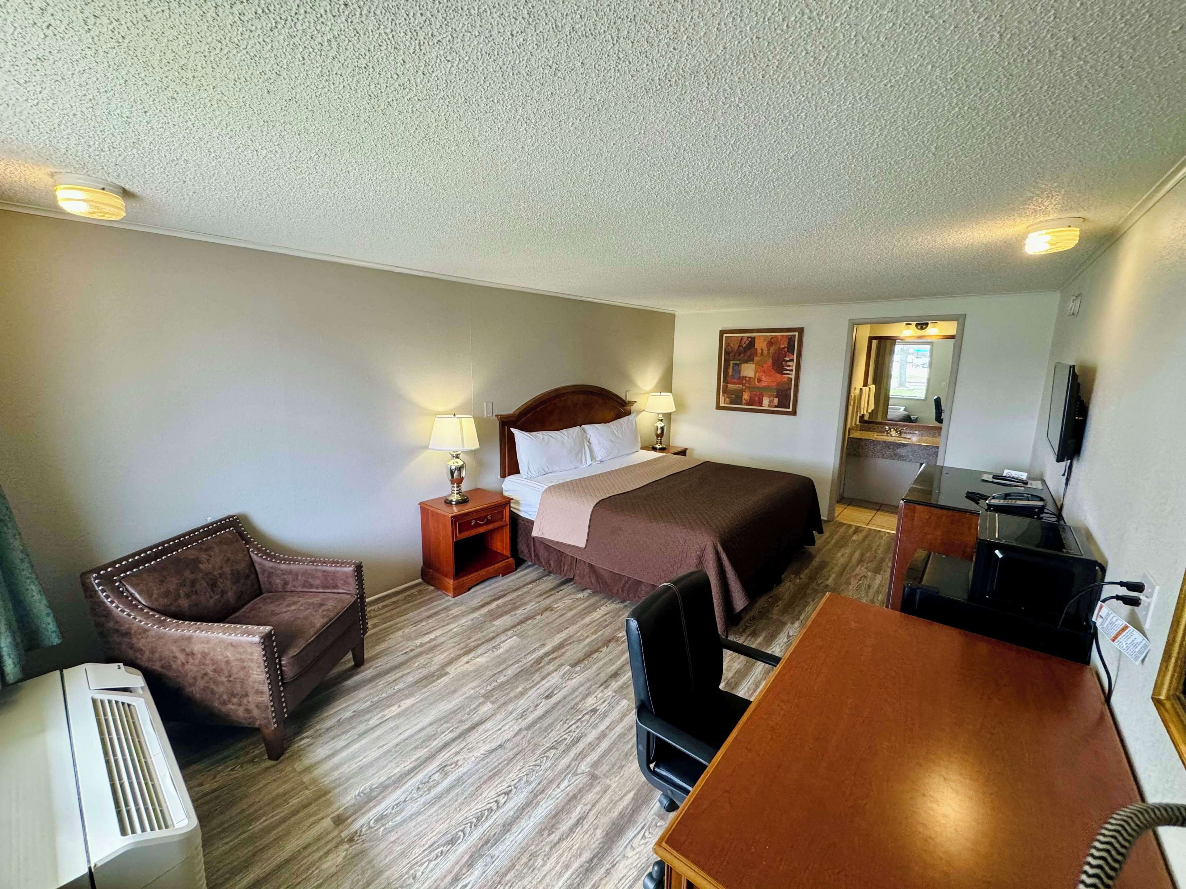 A hotel room with a bed, a desk, a chair, a TV, and a heater.