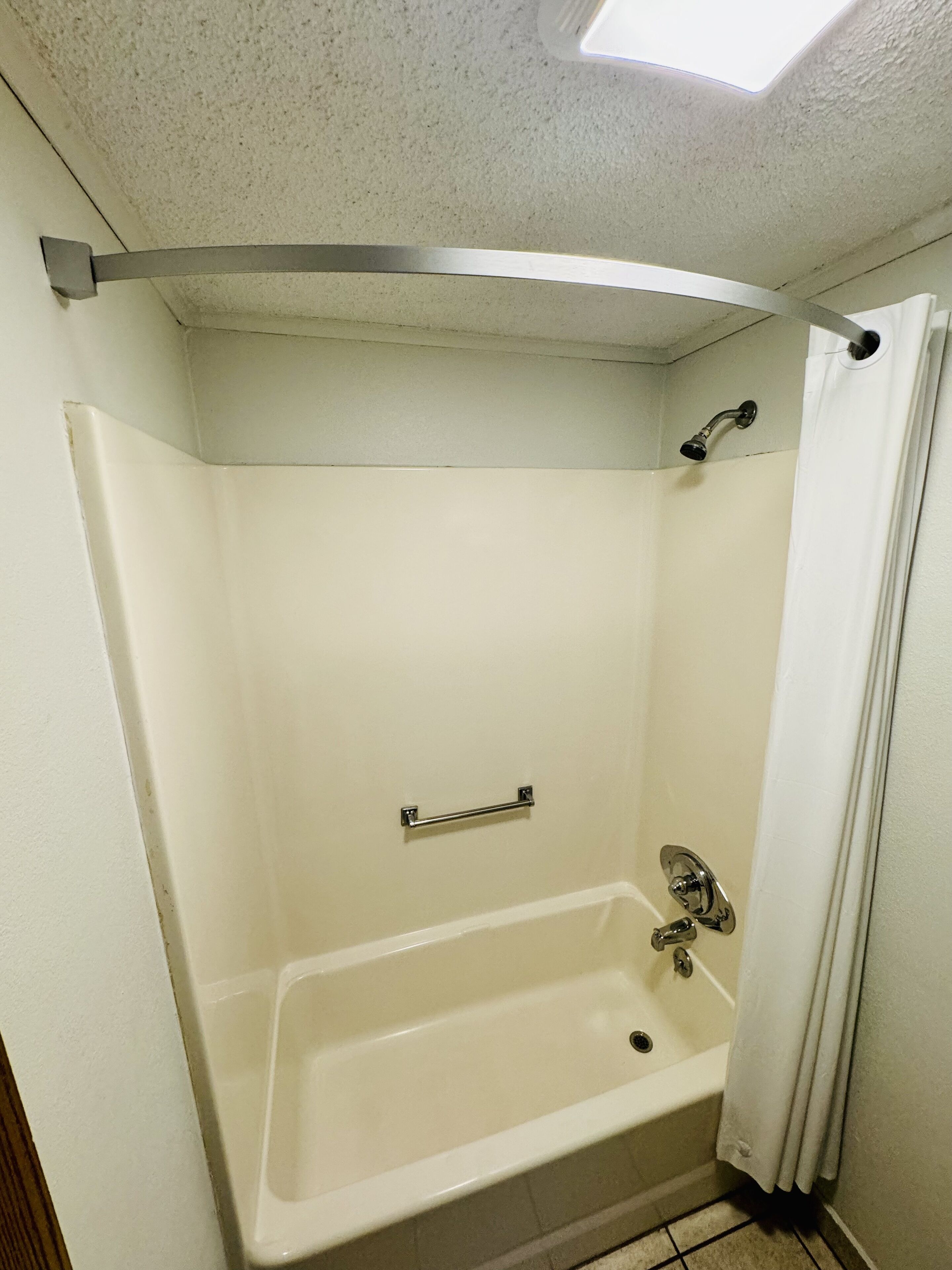 A bathroom with a bathtub, a shower, and a handrail.