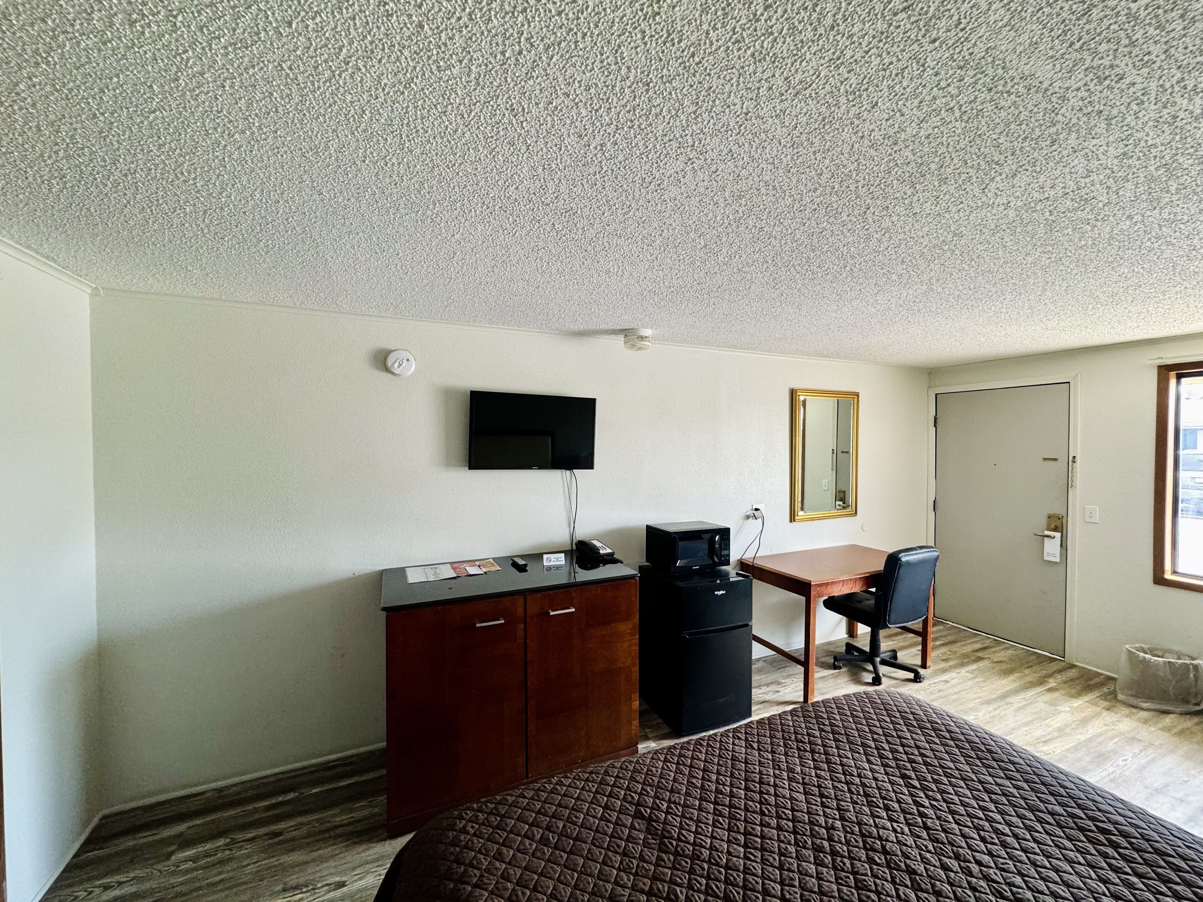 A hotel room with a bed, a desk with a computer, a television, and a mirror.