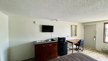 A hotel room with a bed, a desk with a computer, a television, and a mirror.