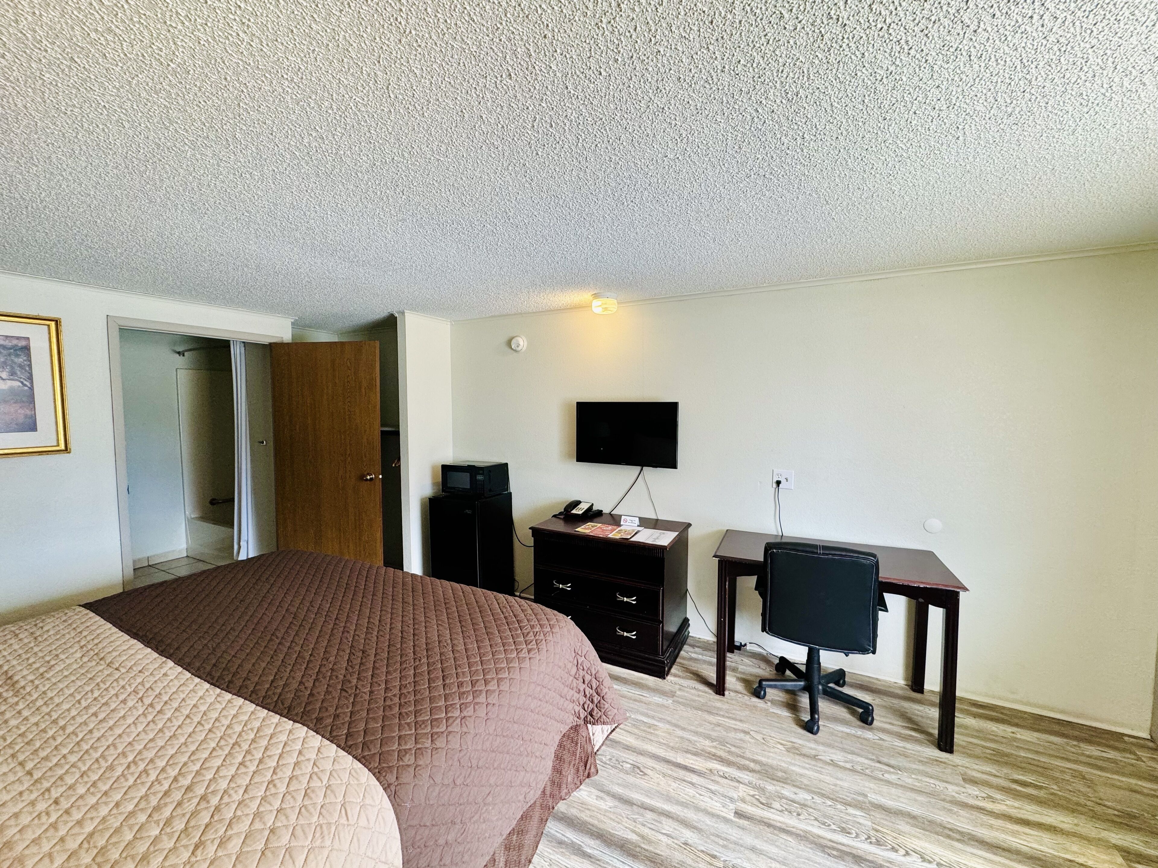 A hotel room with a large bed, a desk with a computer, a TV, and a wardrobe.