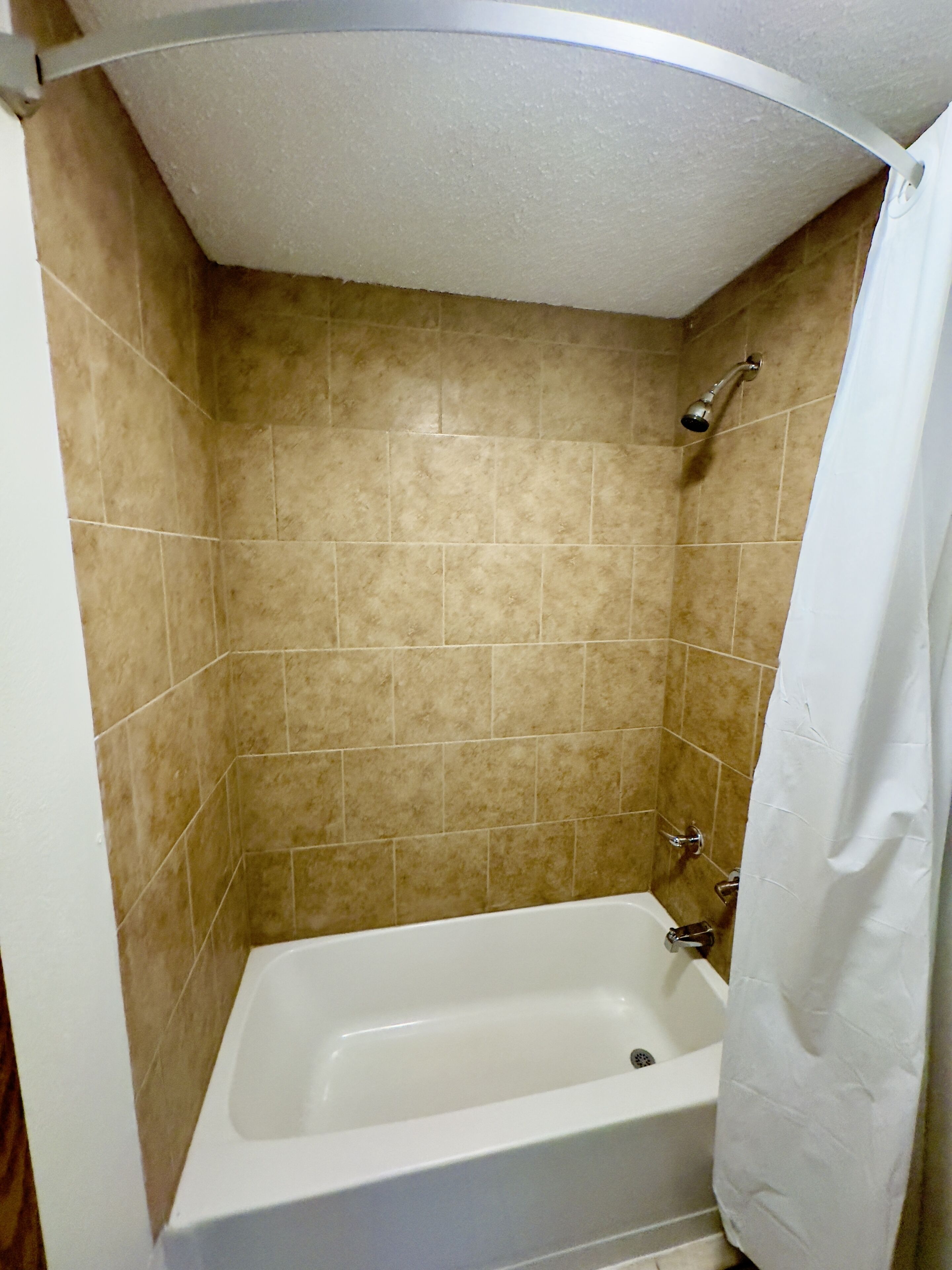 Un baño con azulejos color beige, una bañera blanca y un cabezal de ducha.