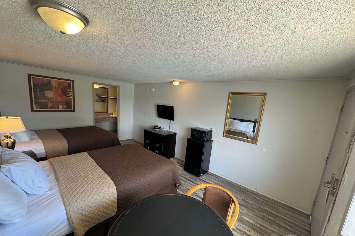 Una camera d'albergo con due letti, una scrivania, una sedia, una televisione, uno specchio e una porta.