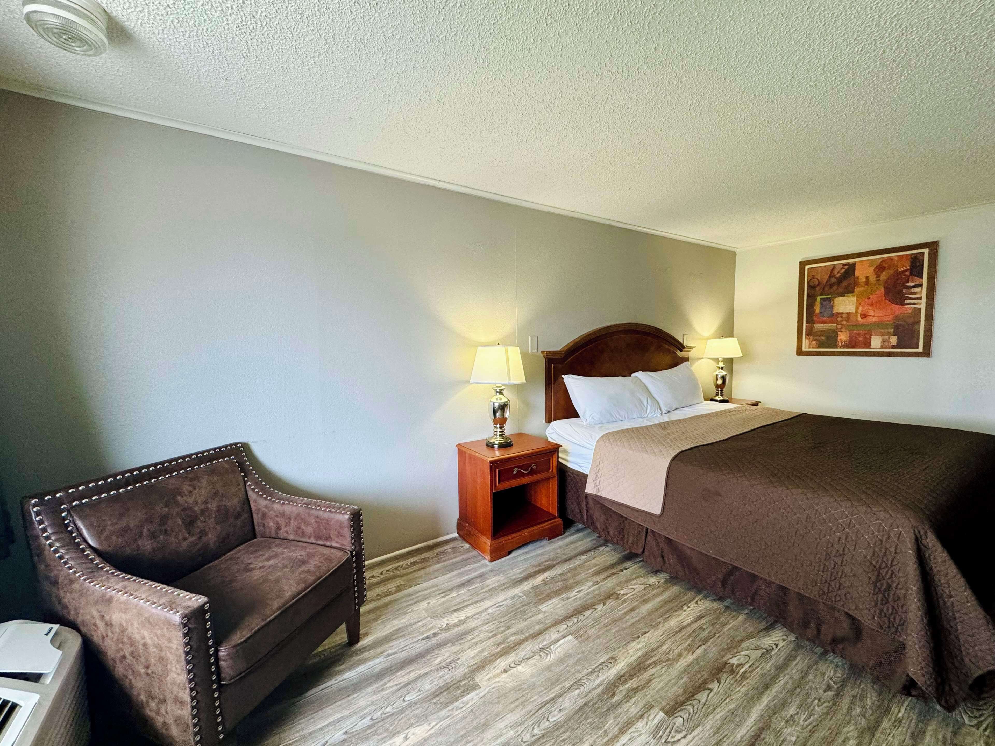 Une chambre d’hôtel avec un lit, une chaise, une table de chevet et un tableau au mur.