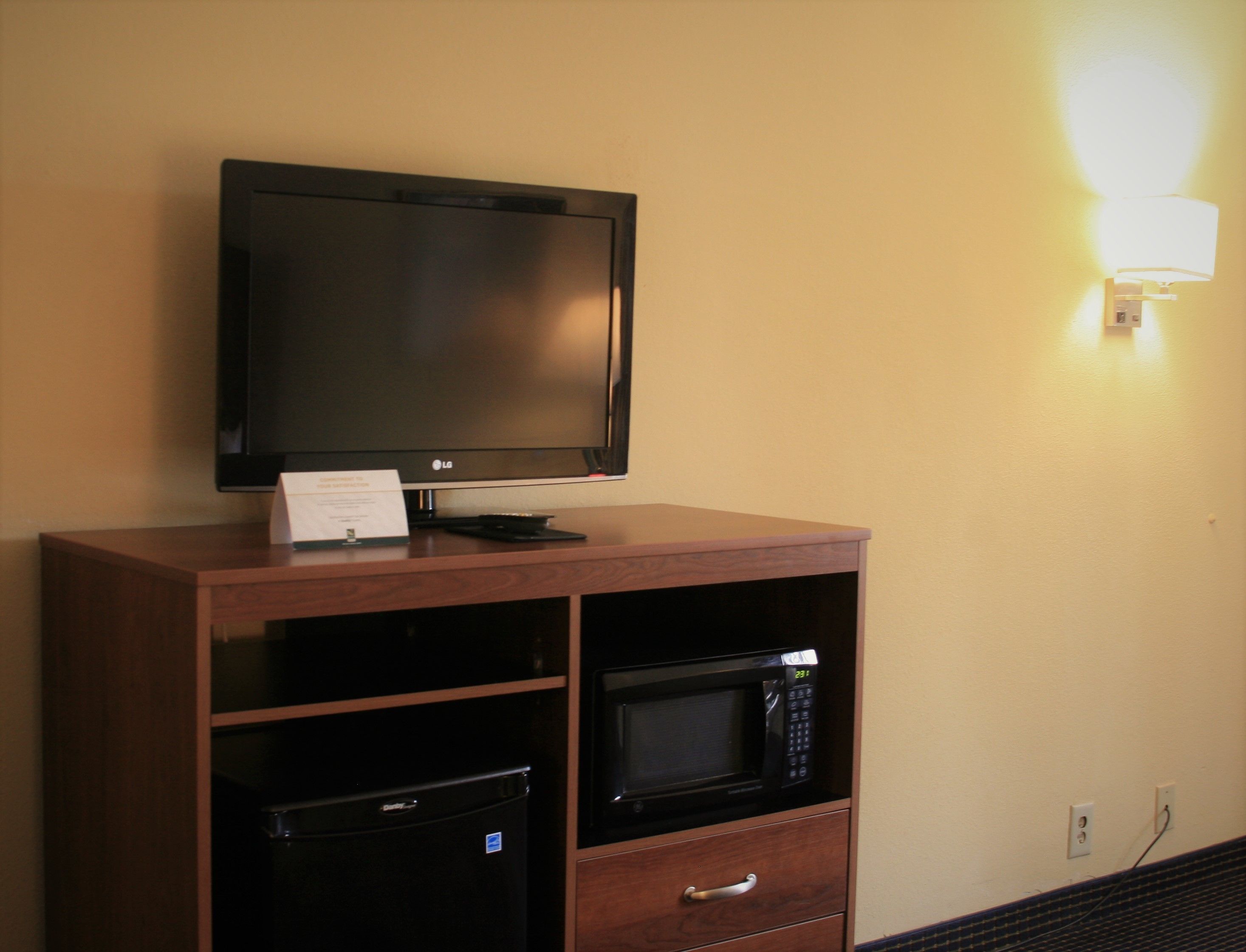 A television on a wooden cabinet, a microwave, and a small refrigerator.