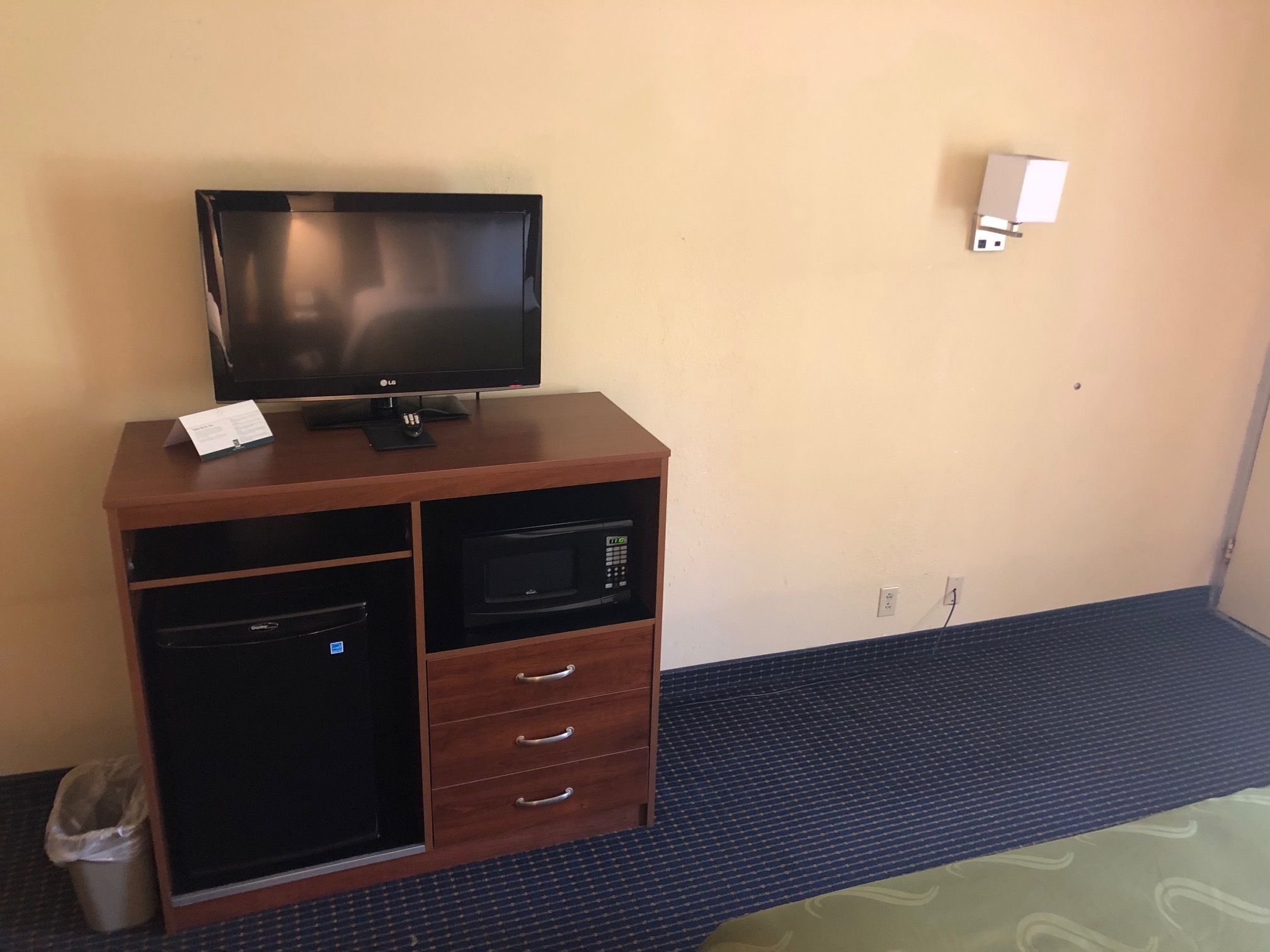 Een hotelkamer met een houten kastje met een televisie, magnetron en prullenbak.