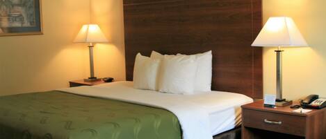 A hotel room with a bed, two bedside lamps, a nightstand with a phone, and a framed picture on the wall.