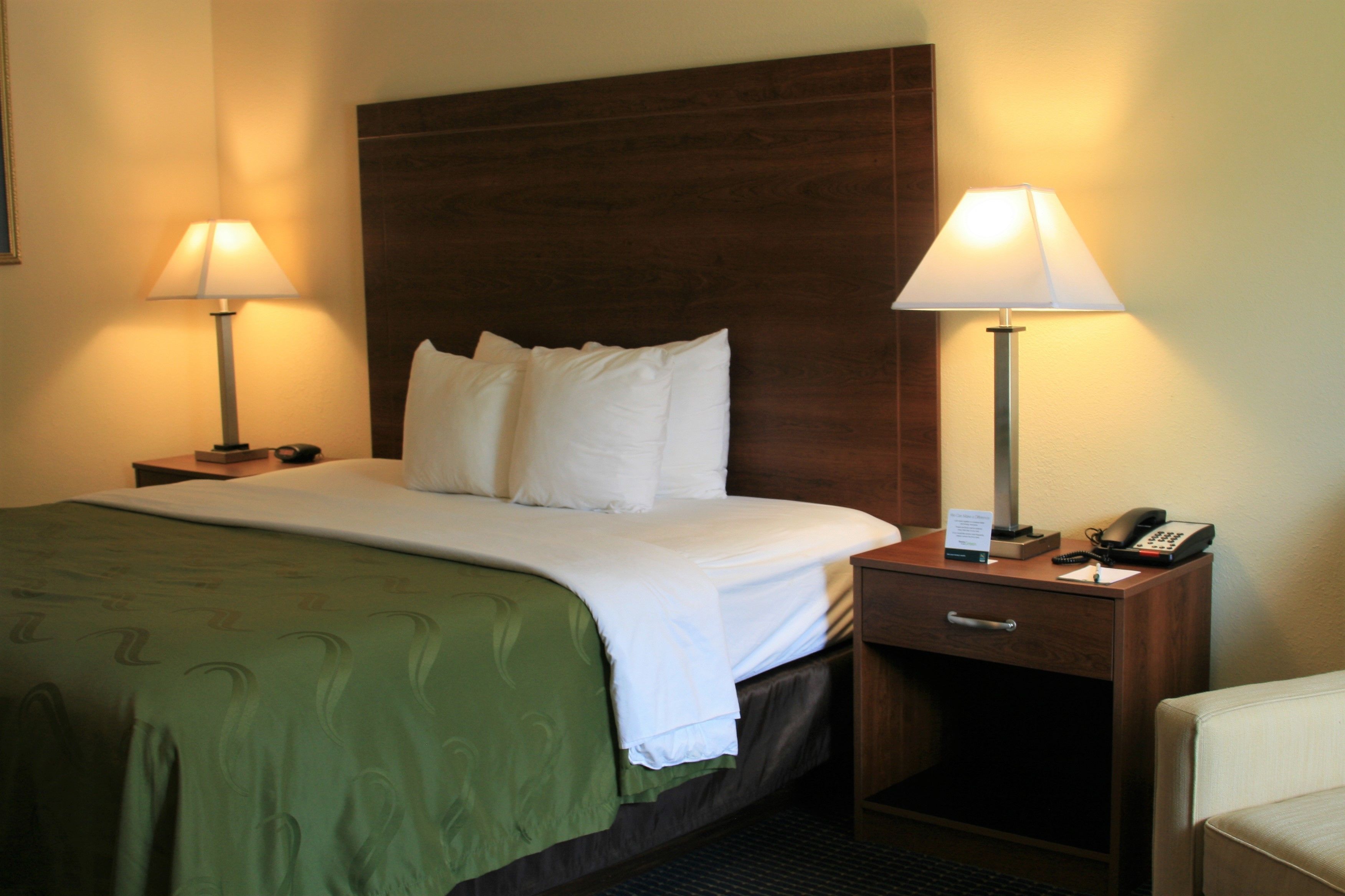 A hotel room with a large bed, two bedside tables with lamps, a wooden headboard, and a small desk with a telephone.