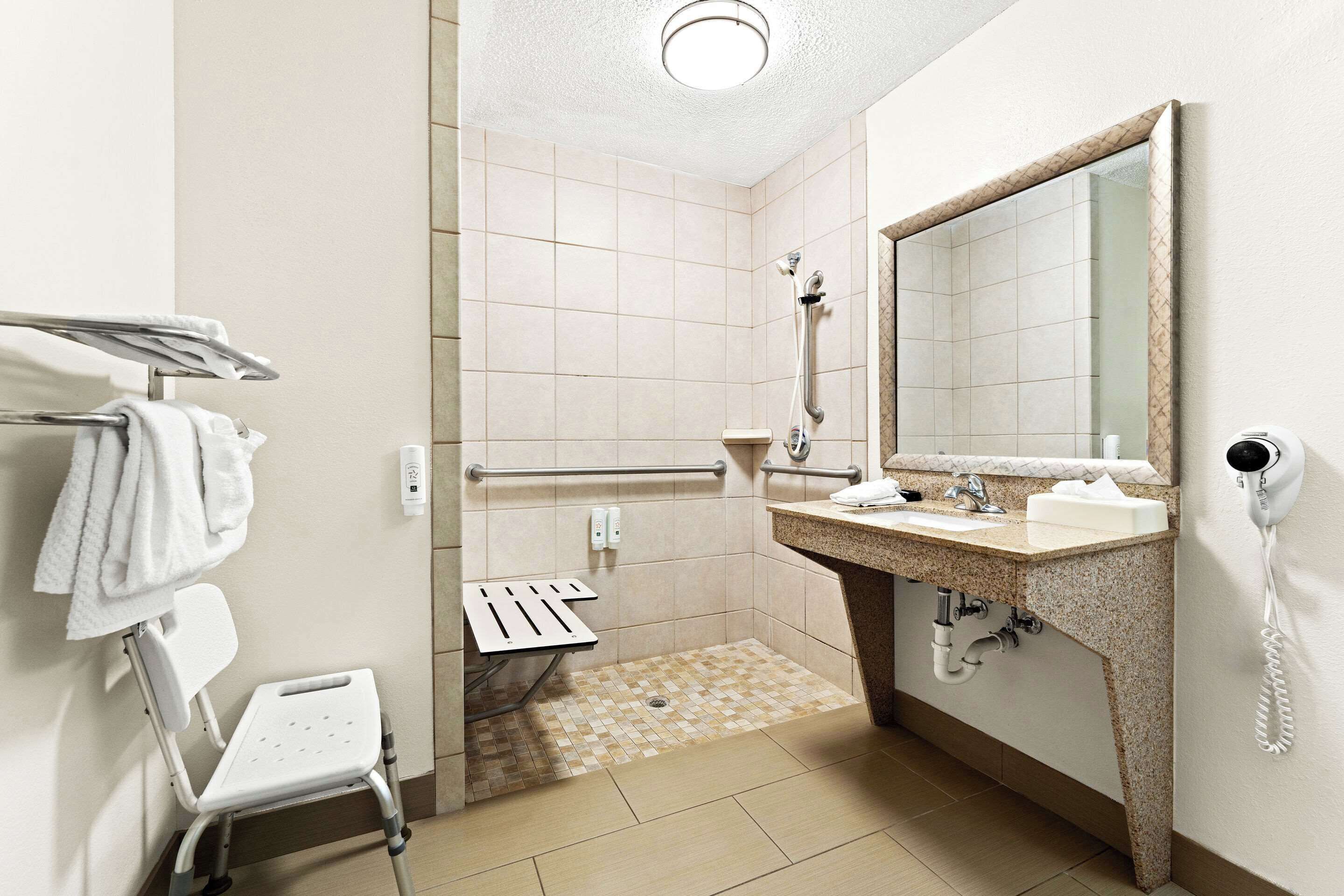 A bathroom with a shower, a sink with a mirror, a towel rack, and a hand dryer.