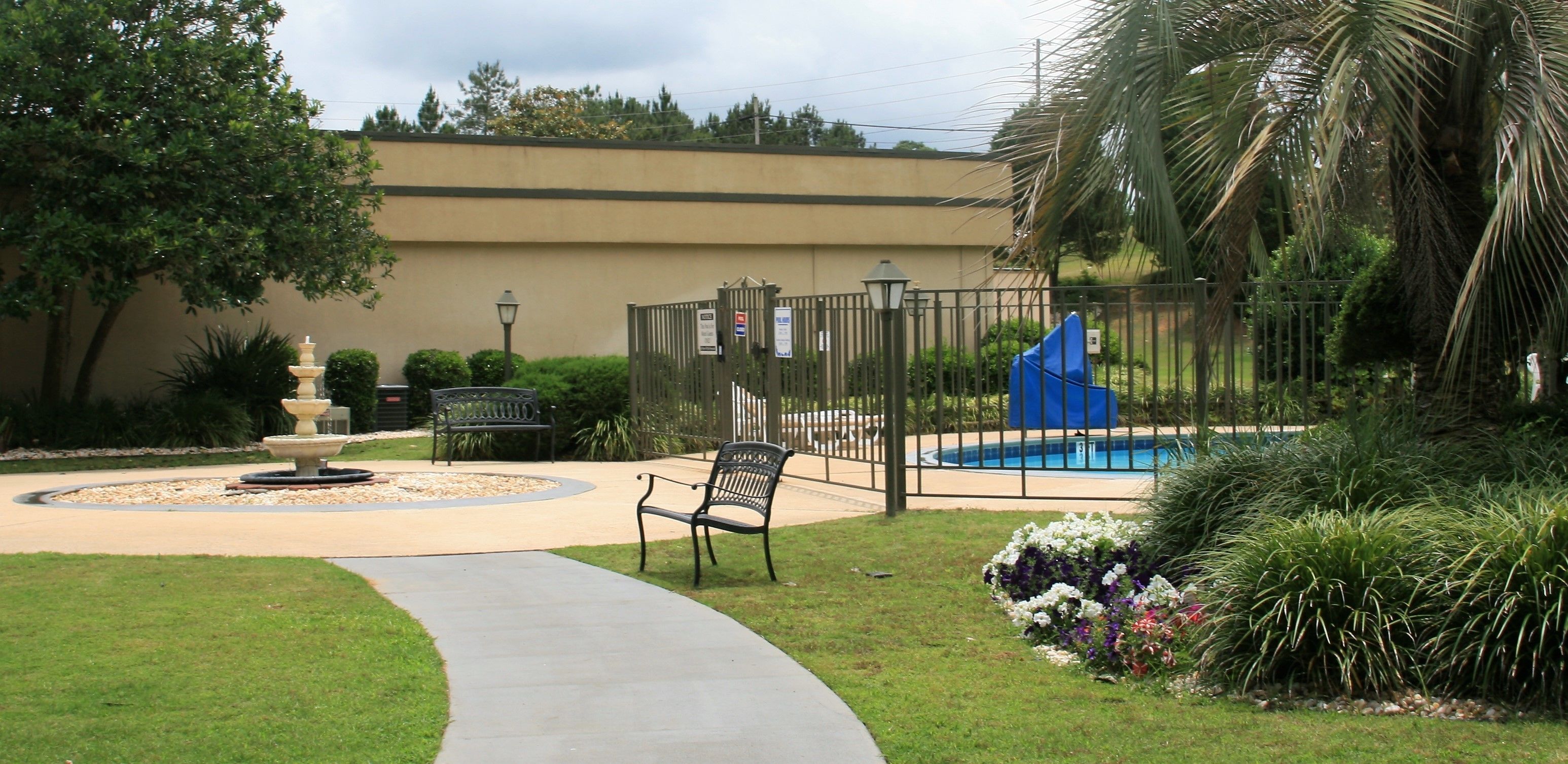 Uma área externa cercada com piscina, bancos e uma fonte.