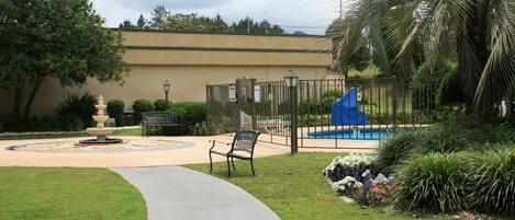 Uma área externa cercada com piscina, bancos e uma fonte.