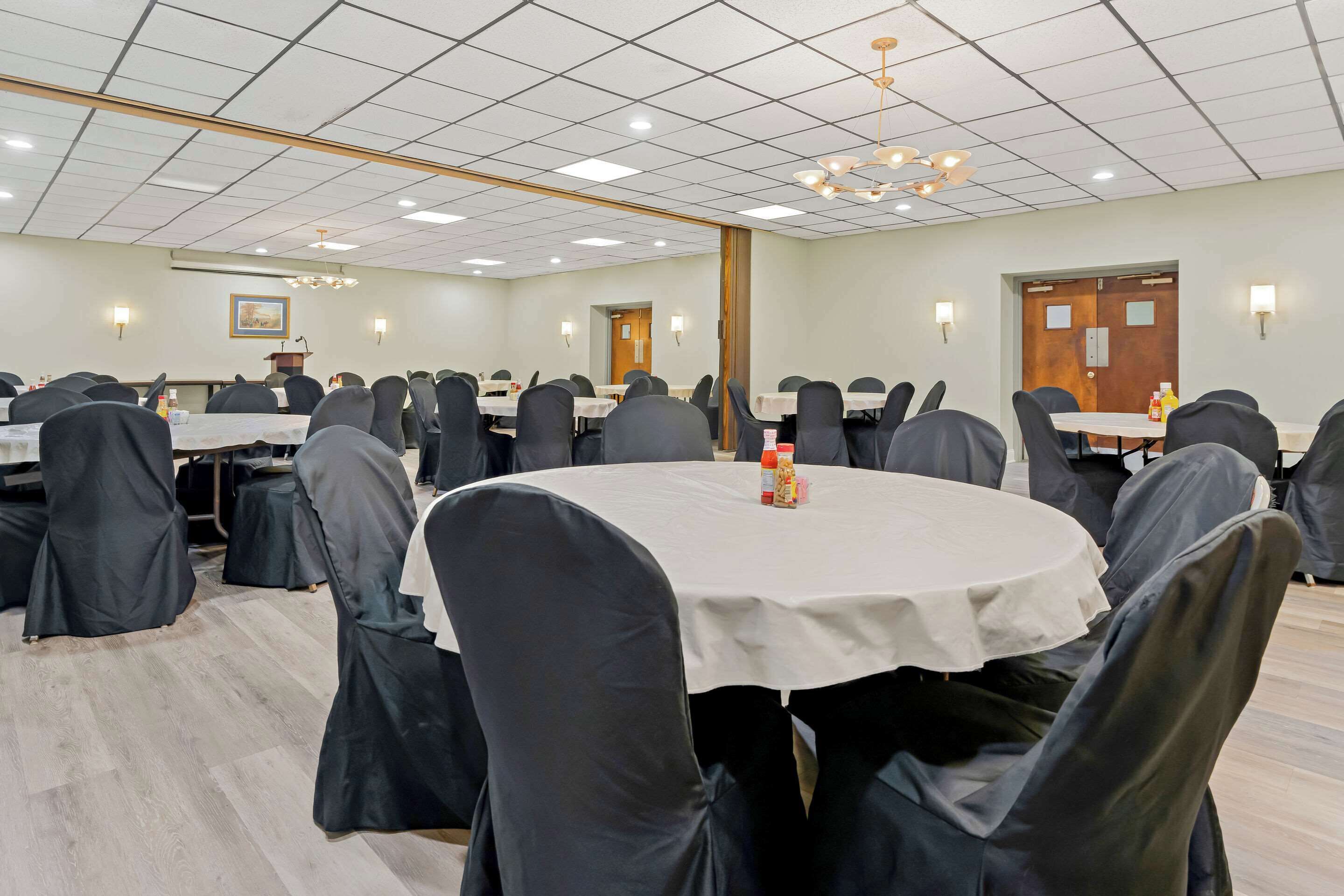 A conference room with round tables, black chairs, and a white tablecloth.