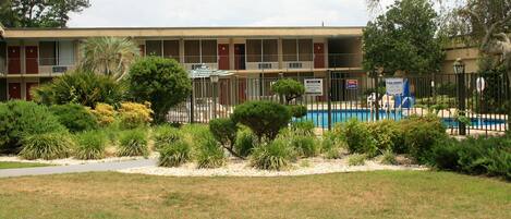 A motel with a swimming pool, fenced area, and various plants in the front yard.