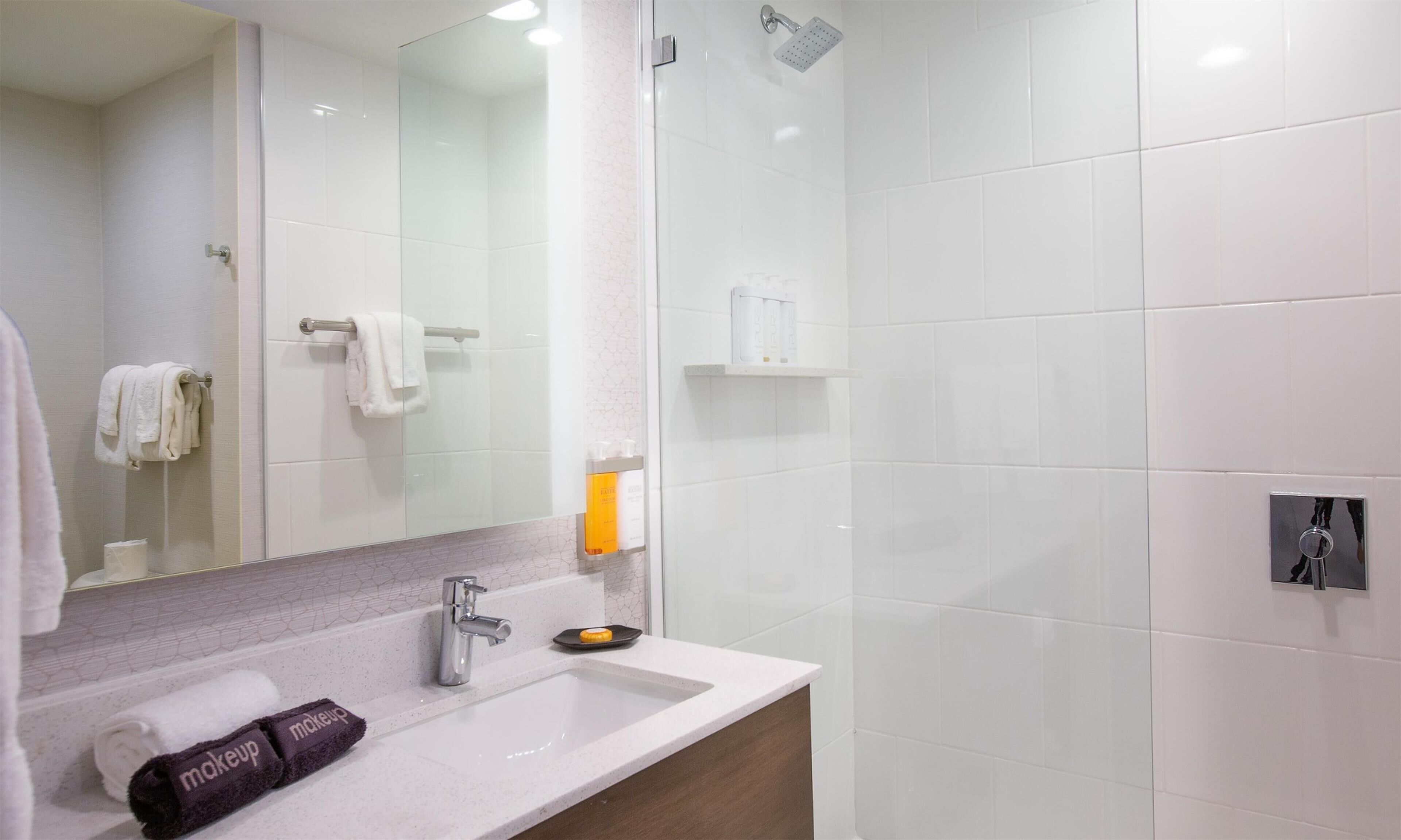 A modern bathroom with a white sink, a mirror, a shower, and a towel rack.
