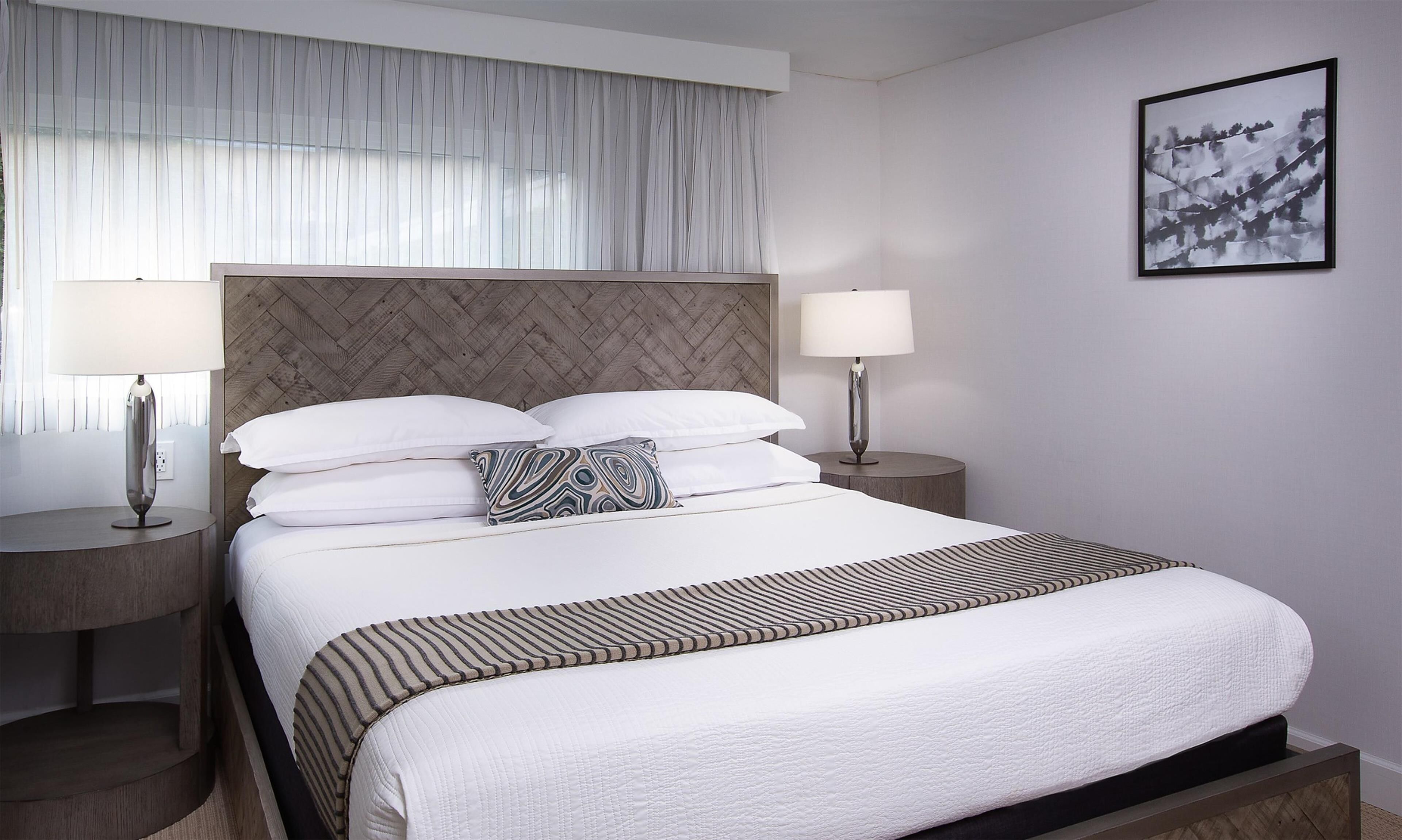 A hotel room with a large bed, two bedside tables, a headboard, and a framed artwork on the wall.